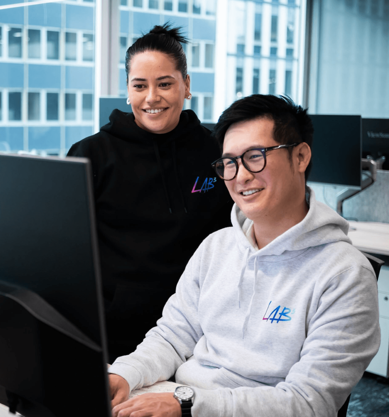 Two LAB3 team members smiling and working together at a desk in the office